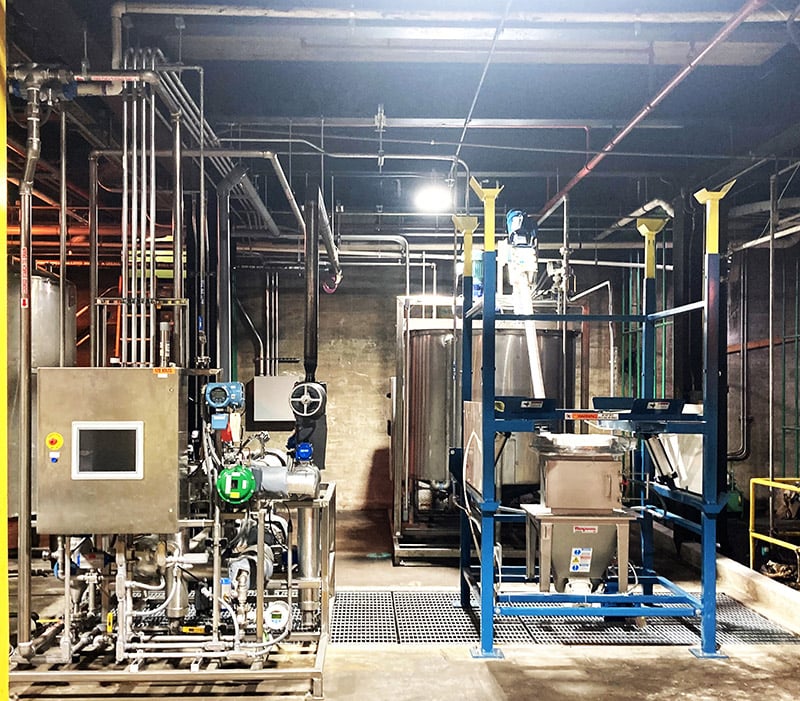 A dry Polyvinyl Alcohol (PVOH) makedown and delivery skid system sits in a manufacturing facility. dry-polyvinyl-alcohol-makedown-skid